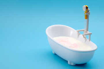 Skin pampering, cosmetic treatment and skincare therapy concept with bathtub filled with milk and pink rose petals isolated on blue background with copy space