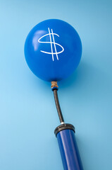 Economic recession, assets bubble and currency inflation concept with manual handpump inflating a balloon with a dollar sign on it isolated on blue background