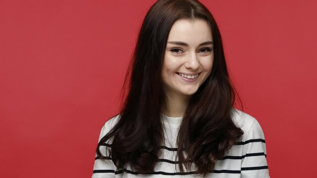 Portrait of woman winking to camera, flirting expression, blinking eye as having cunning idea, wearing casual style long sleeve shirt. Indoor studio shot isolated on red background.