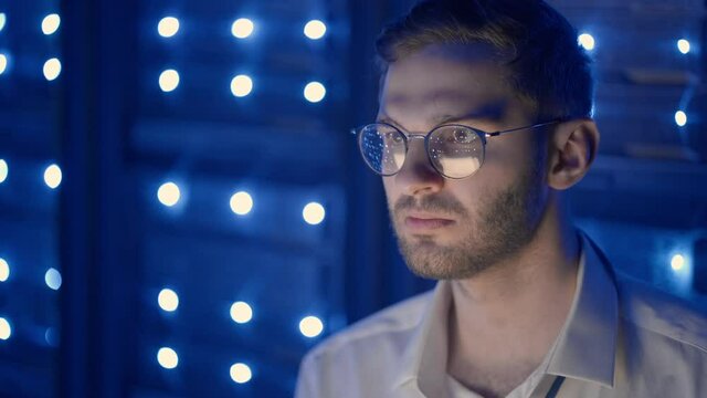 Data center IT specialists coworking in secure server room of cyberspace. Male administrator pointing at error server cabinet running diagnostics on laptop computer
