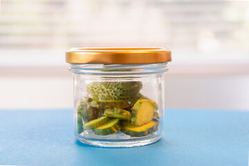 Small cucumbers are sliced in a glass jar.
