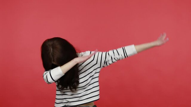 Woman dancing raising hands in dab dance pose, celebrating success, showing gesture of triumph, wearing casual style long sleeve shirt. Indoor studio shot isolated on red background.