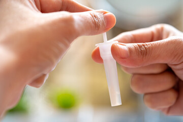 Asian woman using rapid antigen test kit for self test COVID-19 epidemic at home. Adult female unpacking a swab for inserts into her nose. COVID-19 coronavirus pandemic protection concept.