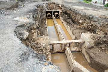Old rusty metal pipes in a pit under the asphalt and sidewalk. Repair of a heating mains and drinking water supply systems in the city