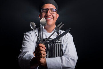 chef holding, kitchen cutlery in foreground, selective focus, with black background,