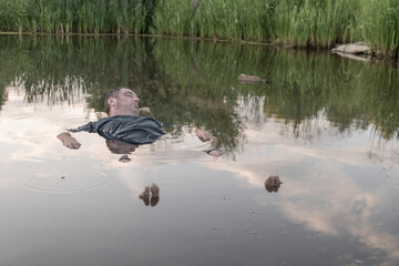 the body of a man who drowned lies face up in the water, the lifeless body of a murdered young man on the river at low tide at sunset