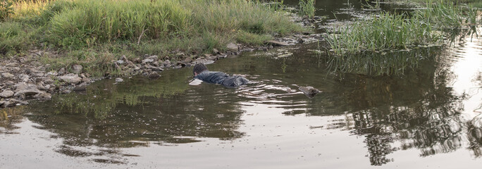 the body of a man who drowned lies face down in the water, the lifeless body of a murdered young man on the river at low tide at sunset