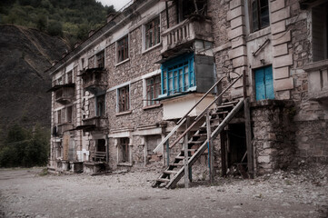 Fototapeta na wymiar Abandoned building in ruined by mudflow old town high in mountains with intricate stonework, ruined balconies, crashed windows. Desolation and destruction