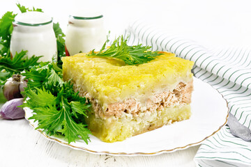 Casserole with potatoes and fish in plate on light board
