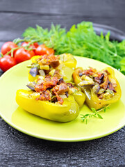 Pepper stuffed with vegetables in green plate on black wooden board