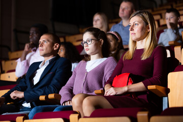 Father, mom and daughter are carefully watching spectacle or concert in the theater auditorium