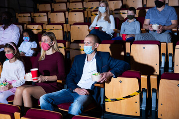 Family with child wearing protective masks eating popcorn and watching a movie in the cinema