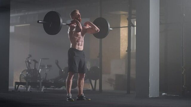 Handsome Muscular Man Does Deadlift and Curls with a Heavy Barbell. Athletic Shirtless Man Training, Doing Power, Strength and Endurance Exercises with Barbell. Workout in the Hardcore Gym
