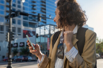 Portrait of woman with jacket, backpack and cell phone in hand in city, concept new beginnings