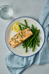 Appetizing healthy baked salmon served on plate. Slices of lemon, a bit asparagus. Glass of water. Healthy diet meal full of protein and omega3 fat. Tasty lunch. Top view, vertical