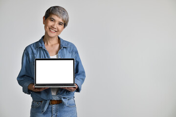 Portrait of middle aged Asian woman 50s wearing casual denim shirt white t-shirt holding laptop computer with blank copy space screen isolated on white background. looking at the camera