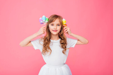 Cute blonde girl 8-9 years old in a white T-shirt and skirt holds Easter eggs isolated on a pink background. Happy Easter, holidays, traditions.