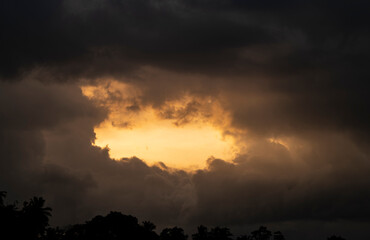 Evening dark clouds gathering in the horizon over the tree line. glowing sunshine passing through the cloud formation.