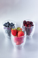 A few transparent glass glasses with strawberries with blueberries and blackberries on a gray background