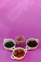 Vertical shot of delicious and healthy sugar free diet yogurt served in a clear glass cup with strawberries with blueberries and blackberries on a pink background