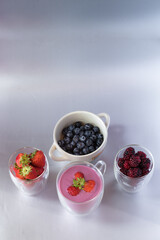 vertical shot of delicious and healthy sugar free diet yogurt served in clear glass cup with strawberries with blueberries and blackberries on a gray background