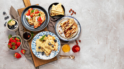 Sweet crepes assortment with berries chocolate on gray background.
