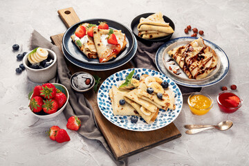 Sweet crepes assortment with berries chocolate on gray background.
