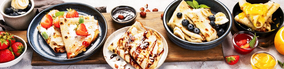 Sweet crepes assortment with berries chocolate on gray background.