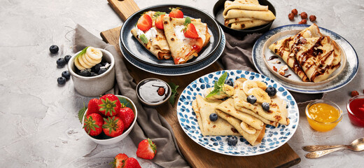 Sweet crepes assortment with berries chocolate on gray background.