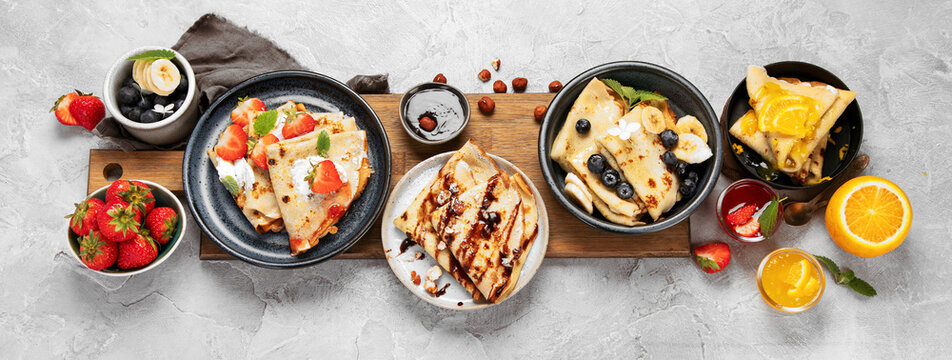 Sweet crepes assortment with berries chocolate on gray background.