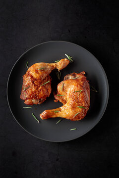 Grilled chicken legs sprinkled with rosemary on a black plate.