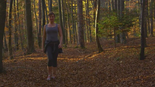 SLOW MOTION, PORTRAIT: Happy young woman walks along a scenic trail in the fall colored forest. Fit Caucasian female strolls along a scenic path in the picturesque woods on a sunny fall evening.