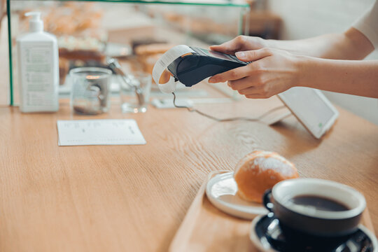 Female barista using terminal for contactless payment in cafeteria