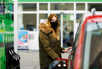 Woman wear medical mask at self-service gas station, hold fuel nozzle, refuel the car with petrol...