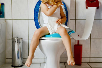 Closeup of cute little toddler baby girl child sitting on toilet wc seat. Potty training for small...