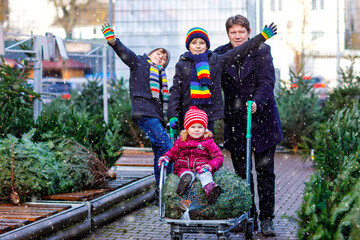 Obraz premium Little toddler girl, two kids boys and father holding Christmas tree on market. Happy family, cute children and middle aged man in winter fashion clothes choosing and buying Xmas tree in outdoor shop.