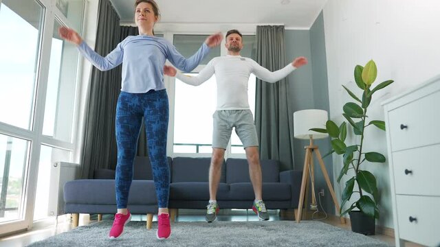Caucasian couple is doing jumping jacks exercise at home in cozy bright room, slow motion.
