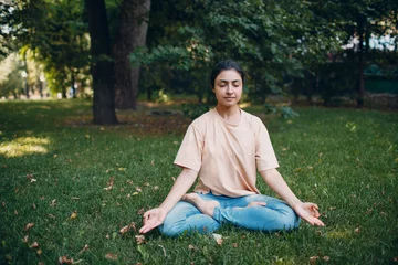 Fotobehang Indian woman doing yoga and meditation in lotus asana pose in outdoor summer park. © primipil