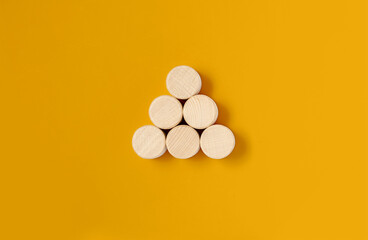 Obraz na płótnie Canvas The circular wooden blocks are placed on a yellow background, the wooden blocks are arranged in a triangular shape. Wood block concept, banner with copy space for text, poster, mockup template.