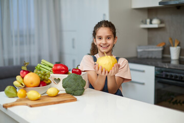 Obraz premium Adorable little girl with curly hair, holding a yellow pumpkin, seated at table in the kitchen.