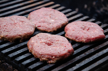 Raw meatballs for burgers are fried on grill. Meat is roasting on BBQ grill outdoor. Heat and smoke dissipate over barbecue.