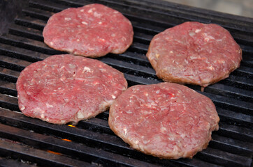 Raw meatballs for burgers are fried on grill. Meat is roasting on BBQ grill outdoor.