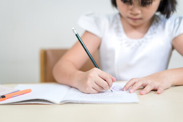 Cheerful Asian little girl children student writing on notebook doing homework and self study at home. Education Homeschool Concept Stock Photo
