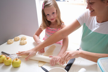 Obraz na płótnie Canvas Smiling mother and daughter roll out dough with rolling pin closeup