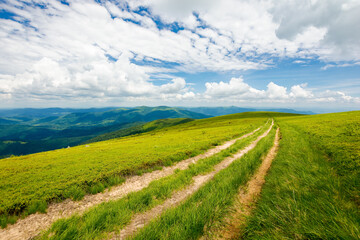 wide trail through grassy meadow. mountain ridge in the distance beneath a gorgeous cloudscape on the blue sky. travel backcountry concept