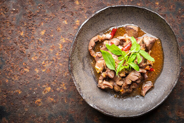 Pad Ka Prao Kruang Nai Gai, Thai food, basil stir fried chicken offal, variety meats, pluck or organ meats in wabi sabi style plate on rusty texture background with copy space for text, top view