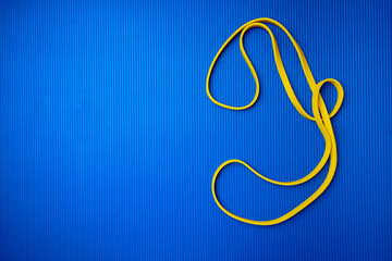 Obraz premium Yellow fitness rope on blue mat background