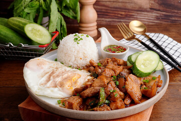 Crispy pork basil rice with fried egg, spicy food, in a round plate on the wooden floor.
