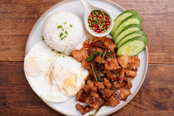 Crispy pork basil rice with fried egg, spicy food, in a round plate on the wooden floor.