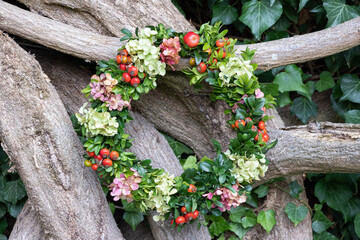 Blumenkranz mit Hortensien-Blüten, Hagebutten und Buchs hängend am Ast